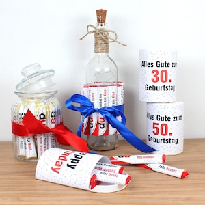 May include: A birthday gift idea featuring a glass bottle filled with candy bars, wrapped with a blue ribbon, and two white cardboard tubes with the text "Alles Gute zum 30. Geburtstag" and "Alles Gute zum 50. Geburtstag".