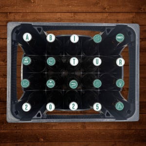 May include: A black crate filled with brown glass bottles. Each bottle has a green cap with a different design. The caps have text and symbols, including "ABITUR", "AUF DICH!" and "PROST!"