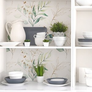 May include: White shelves with a watercolor floral wallpaper featuring green leaves and gold accents. The shelves are decorated with white dishes, a white pitcher, and small potted plants.