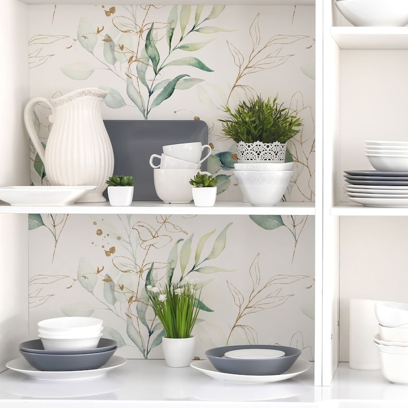 May include: White shelves with a watercolor floral wallpaper featuring green leaves and gold accents. The shelves are decorated with white dishes, a white pitcher, and small potted plants.