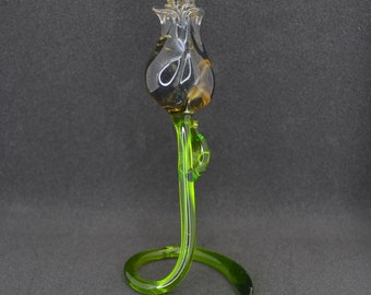 May include: A glass rose sculpture with a clear, swirling glass stem and a dark green base. The rose is made of clear glass with a dark brown center.