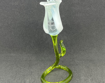 May include: A glass rose sculpture with a white frosted flower and a green stem and base.