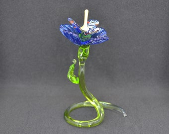 May include: A handcrafted glass flower sculpture with a blue and green color scheme. The flower has a blue blossom with red and white accents, a green stem, and a coiled base. The sculpture is approximately 6 inches tall.