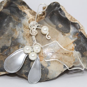 May include: A silver wire-wrapped Christmas ornament featuring a mistletoe design with white pearl beads. The ornament is displayed on a piece of rough, gray rock.
