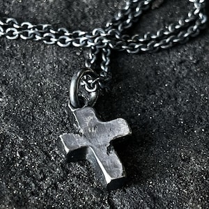 May include: A silver chain necklace with a simple, chunky, silver cross pendant.