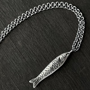 May include: A silver chain necklace with a detailed silver fish pendant.