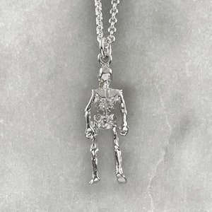 May include: A silver skeleton pendant necklace. The pendant is detailed and features a skeletal figure with visible ribs and bones.