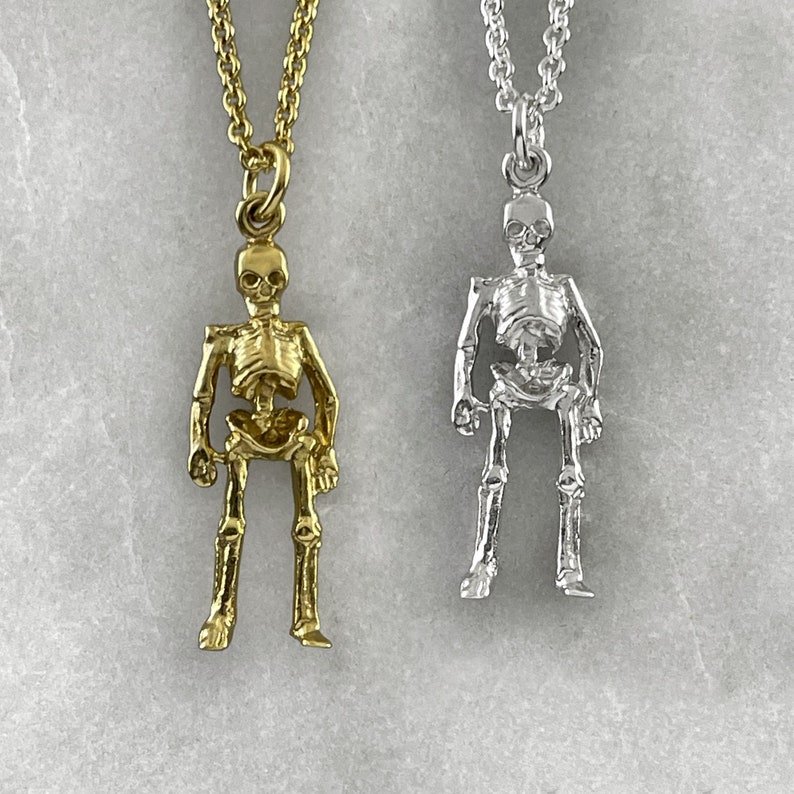 May include: Two skeleton pendant necklaces, one gold and one silver. The skeletons are detailed and have a realistic look.