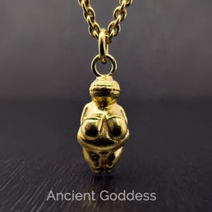 May include: A gold-coloured pendant necklace featuring a stylised figurine of an ancient goddess. The pendant is suspended from a matching chain. The text "Ancient Goddess" is at the bottom of the image.