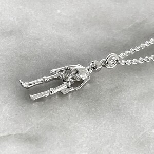 May include: A silver skeleton pendant necklace. The pendant is a detailed, three-dimensional skeleton figure with a chain link attached to the top of the skull.