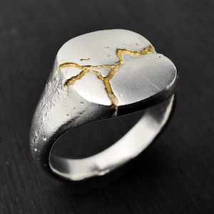 May include: A silver ring with a cracked oval top. The cracks are filled with gold.