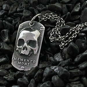 May include: A silver pendant necklace featuring a skull design and the inscription "Memento Mori".