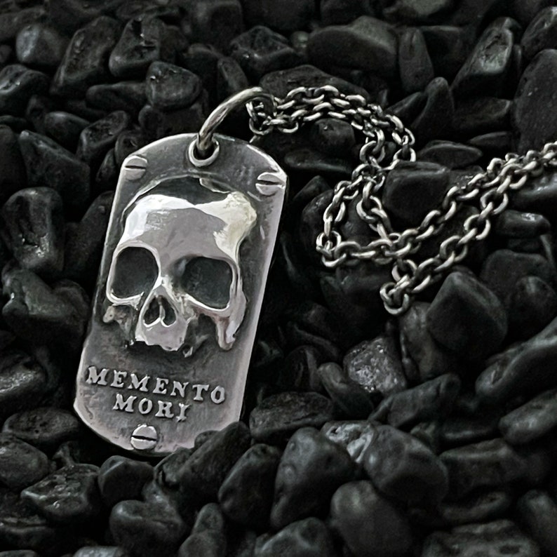 May include: A silver pendant necklace featuring a skull design and the inscription "Memento Mori".