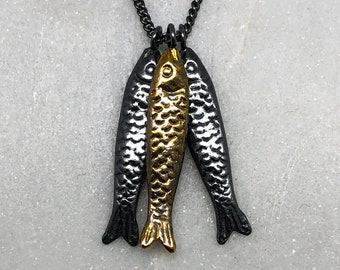 Könnte beinhalten: Eine silberne Kettenkette mit einem Anhänger aus drei Fisch-Anhängern. Der mittlere Fisch ist golden, die beiden äußeren Fische sind silber.