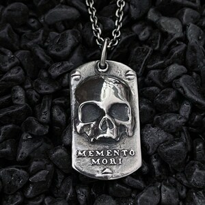 May include: Silver pendant necklace featuring a skull design and the inscription "Memento Mori".