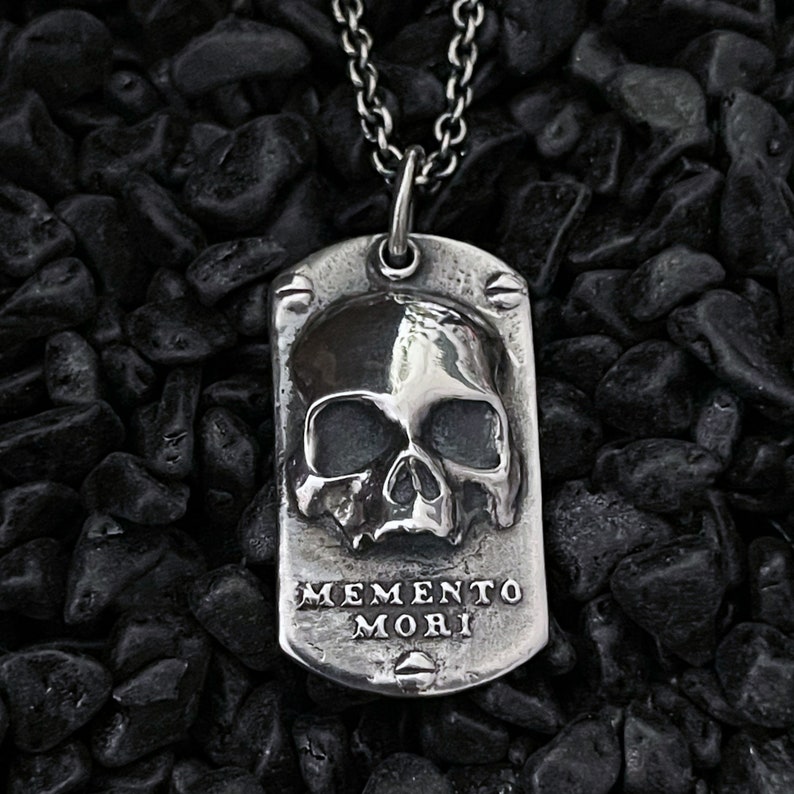 May include: Silver pendant necklace featuring a skull design and the inscription "Memento Mori".