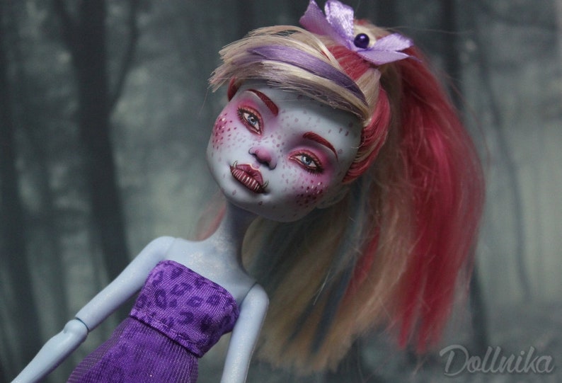 May include: A custom-made doll with blue skin, pink and white hair, and purple clothing. The doll has a painted face with pink blush and blue eyes.