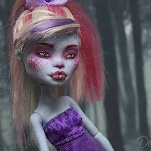 May include: A custom-made doll with pink and blonde hair, blue eyes, and purple and white clothing. The doll has a pale blue complexion and pink freckles.