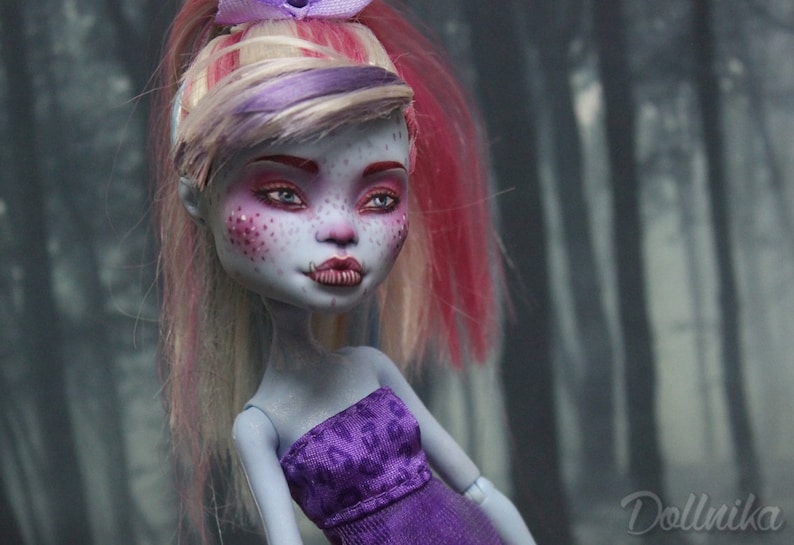 May include: A custom-made doll with pink and blonde hair, blue eyes, and purple and white clothing. The doll has a pale blue complexion and pink freckles.