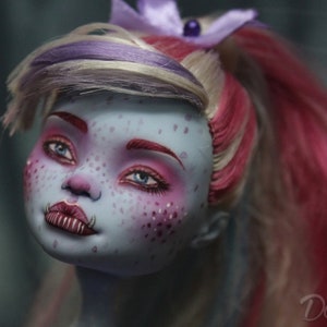 May include: A blue-skinned doll with pink and white hair, wearing pink eyeshadow and lipstick. The doll has a nose ring and fangs.