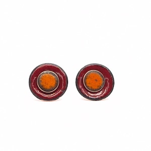 May include: A pair of red and orange enamel earrings with a circular design. The earrings have a silver backing.