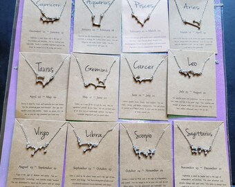 May include: Twelve silver necklaces with zodiac signs and birth dates on brown cards. The signs are Capricorn, Aquarius, Pisces, Aries, Taurus, Gemini, Cancer, Leo, Virgo, Libra, Scorpio, and Sagittarius.