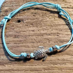 May include: A light blue ankle bracelet with a silver turtle charm and silver beads.