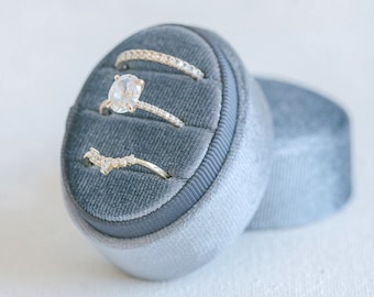 May include: Three gold rings with diamonds set in a gray velvet ring box. The rings are stacked on top of each other.