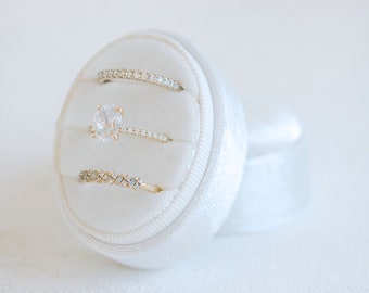 May include: Three gold rings with diamonds set in a white velvet ring box. The center ring features a larger oval-shaped diamond.