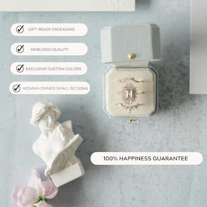 May include: A light blue velvet ring box displaying three gold rings. The rings feature a central stone and surrounding smaller stones. The box is open, revealing a cream-coloured interior. Text on the image reads: Gift-Ready Packaging, Heirloom Quality, Exclusive Custom Colors, Woman-Owned Small Biz (USA), and 100% Happiness Guarantee.