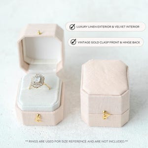 May include: Two octagonal blush-coloured ring boxes, one open and one closed. The open box displays a ring with a gold band and a square, multi-faceted stone. Text on the image reads: "LUXURY LINEN EXTERIOR & VELVET INTERIOR" and "VINTAGE GOLD CLASP FRONT & HINGE BACK."