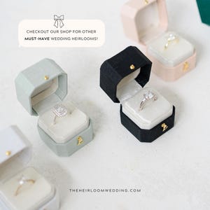May include: Several open ring boxes in various colors, including black, pink, and green, each displaying a different engagement ring. The boxes are octagonal and lined with white velvet. Text in the image reads: "CHECKOUT OUR SHOP FOR OTHER MUST-HAVE WEDDING HEIRLOOMS!"