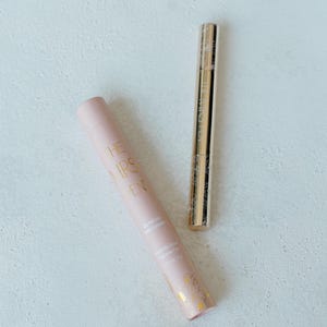 K&ouml;nnte beinhalten: Zwei Kosmetikprodukte, eine rosa Tube mit goldener Beschriftung, die "The Good Skin Cleanser" lautet, und eine goldene Tube mit goldener Beschriftung, die "The Wholeher" lautet.