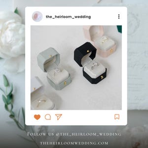 May include: A selection of open ring boxes in shades of grey, black, and pink, each showcasing a diamond ring. The boxes are presented on a white surface. The text "FOLLOW US @THE_HEIRLOOM_WEDDING" and "THEHEIRLOOMWEDDING.COM" are visible.