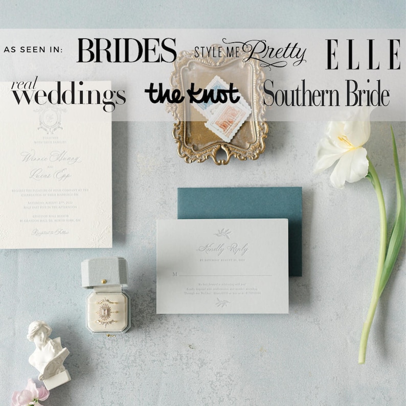 Op de afbeelding: Bruiloft briefpapier set met een uitnodiging, antwoordkaart en envelop in zachte witte en blauwe tinten. Een kleine ringdoos en een decoratief dienblad met postzegels zijn ook inbegrepen. Een witte bloem en een kleine buste.