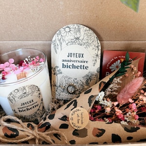Op de afbeelding: Een geschenkdoos met een glazen kaars met roze en witte droogbloemen, een kaart met de tekst JOYEUX anniversaire bichette, een armbandje en een boeket droogbloemen in luipaardprint papier met een handmade with love sticker.