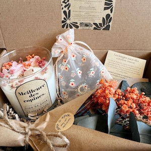 Peut inclure: Un coffret cadeau contenant une bougie en verre avec une étiquette Meilleure des copines, un sachet en organza transparent à motifs floraux, et un bouquet de fleurs séchées orange et feuilles d'eucalyptus enveloppé dans du papier kraft.