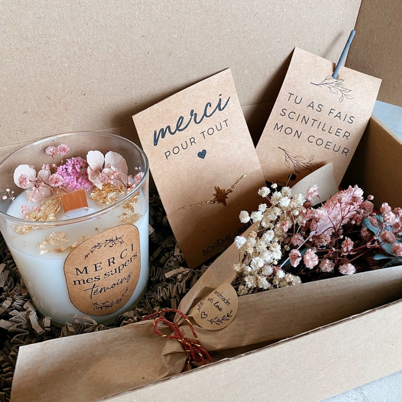 May include: A gift box filled with a white candle with dried flowers and gold flakes, a gold necklace with a star charm, a small bouquet of dried flowers, and two cards with the text "merci pour tout" and "tu as fais scintiller mon coeur".