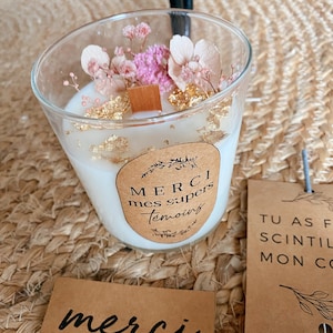 May include: A white candle with a brown label that says "Merci mes supers temoins". The candle is decorated with dried flowers and gold flakes.
