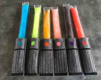 May include: Six gray felt lightsaber holders with different colored popsicles inside. The holders have a black embroidered design and a colored circle on the front.