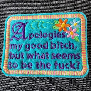May include: A rectangular turquoise embroidered patch with a multi-colored striped border. The text reads: Apologies my good bitch, but what seems to be the fuck? The design includes embroidered orange, pink, and blue flowers with green leaves.