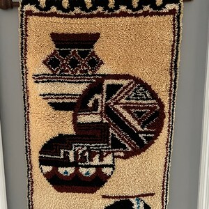 May include: A beige wall hanging with a brown, black, and white geometric design. The design features three round shapes with a bear at the bottom.