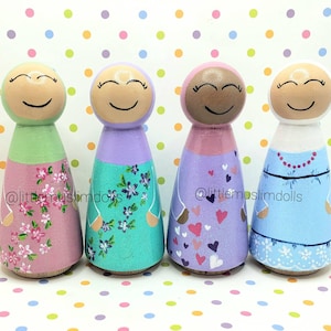 May include: Four wooden peg dolls dressed in colorful clothing with floral and heart patterns. The dolls are wearing headscarves and have smiling faces. The dolls are standing on a white background with colorful polka dots.