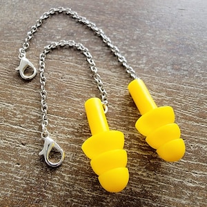 May include: A pair of yellow silicone earplugs with a silver chain connecting them. The earplugs have a layered design and are connected by a silver chain with a clasp.
