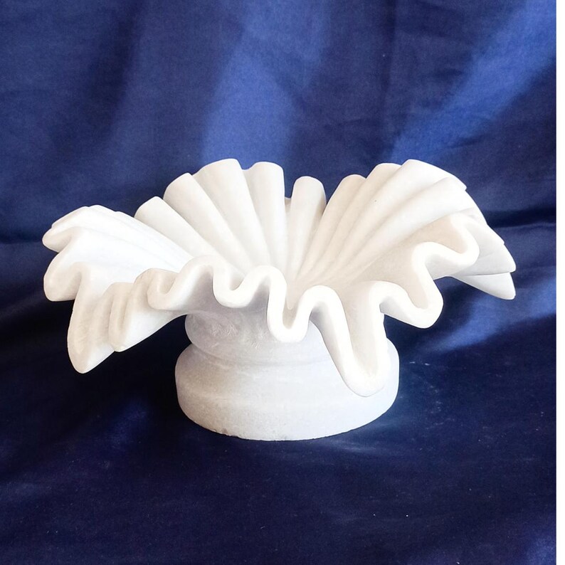 May include: White marble bowl with a ruffled edge, resembling a flower. The bowl is on a white marble pedestal.
