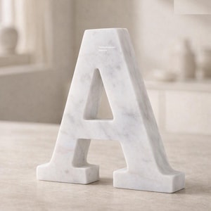 May include: A freestanding letter A crafted from white marble with grey veining. The surface features a smooth, polished finish. The text "Rameshwaram Marble" is printed in small, light-colored letters on the upper center of the letter A.