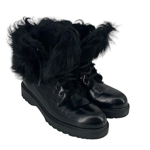 May include: A pair of black leather boots with a thick sole and lace-up closure. The boots feature a fluffy black fur trim around the top. The boots are set against a white background.