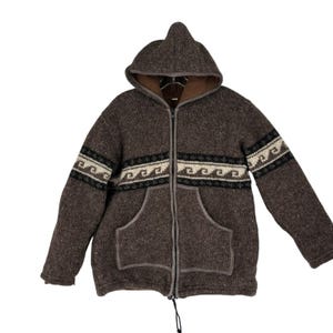 May include: A brown hooded jacket with a zipper closure and two front pockets. The jacket features a decorative band of white, black, and tan geometric patterns across the chest and sleeves. The hood is lined with a lighter brown fabric.