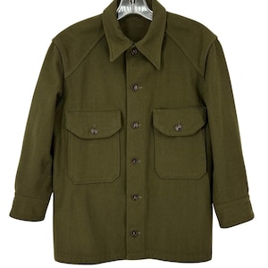 May include: Olive green wool jacket with a button-up front, two chest pockets, and a collared neckline. The jacket has long sleeves and a classic, utilitarian design. The buttons are a dark brown color. The jacket is made of a thick wool material.