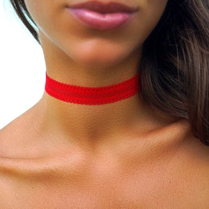 May include: A close-up of a person wearing a red lace choker necklace. The choker is thin and delicate, with a simple design.